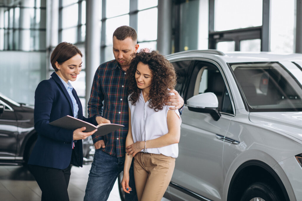 Young couple talking to a sales person in a car showroom -